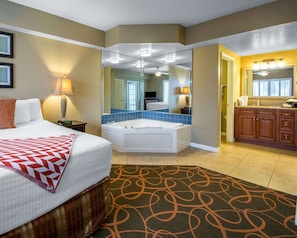 A hotel room with a bed, a bathroom with a bathtub, and a separate bathroom with a sink and mirror.