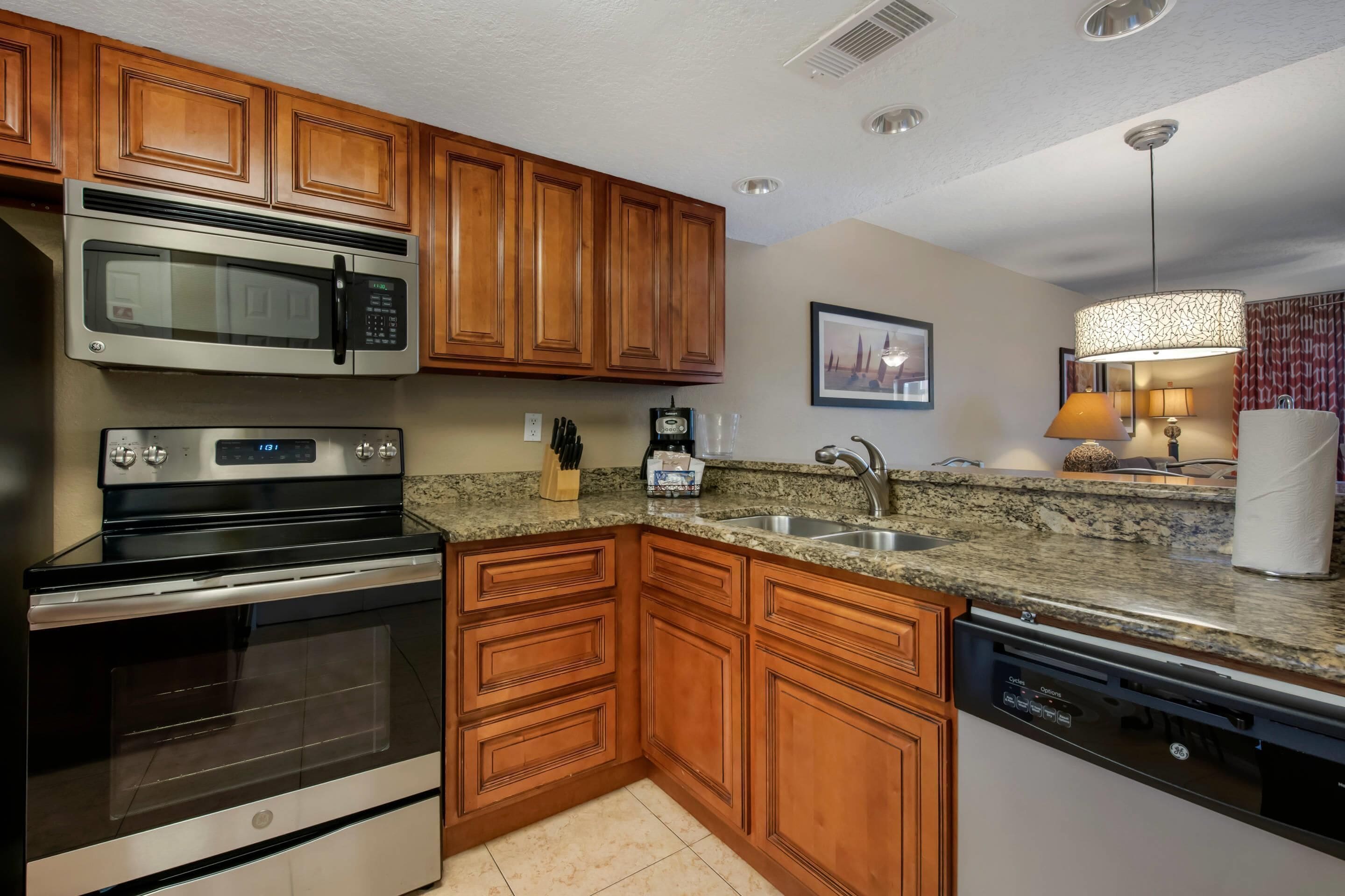 A kitchen with wooden cabinets, a stainless steel microwave, an oven, a dishwasher, granite countertops, a sink, and a pendant light.