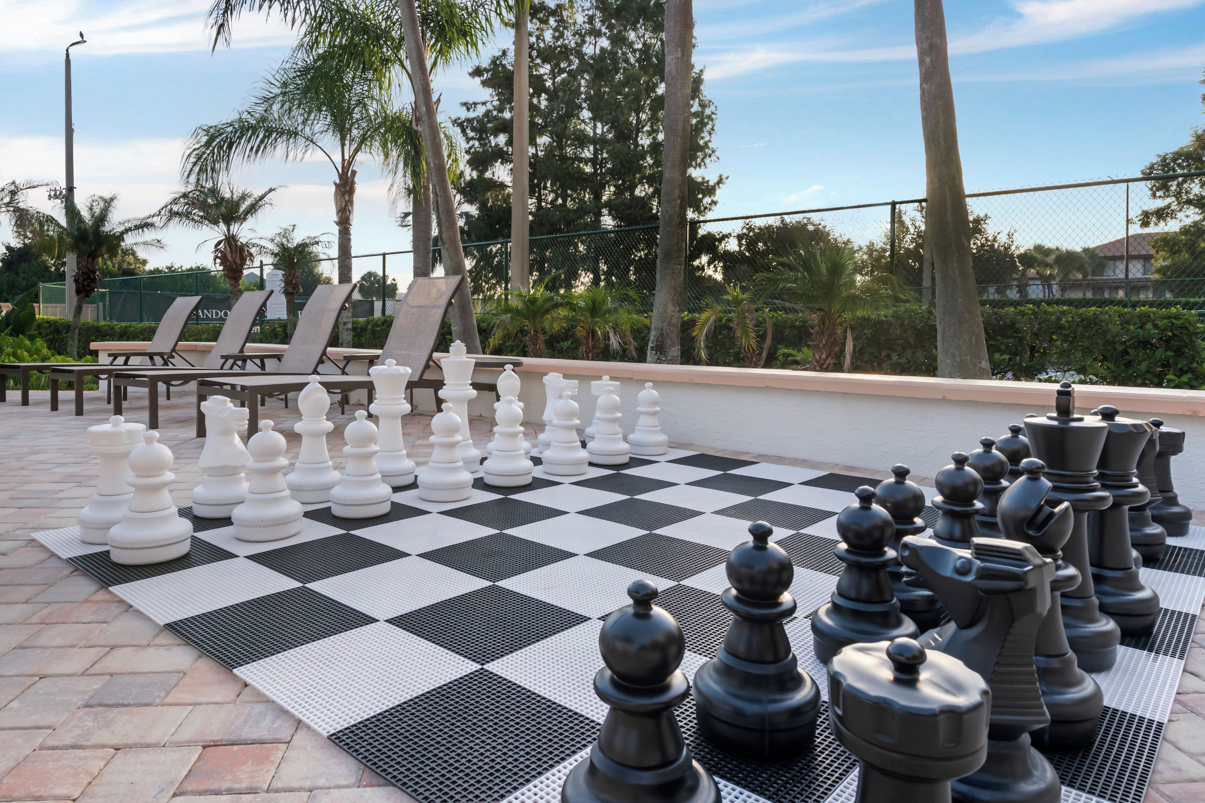 Un jeu d’échecs installé sur une terrasse, avec des fauteuils et des palmiers en arrière-plan.