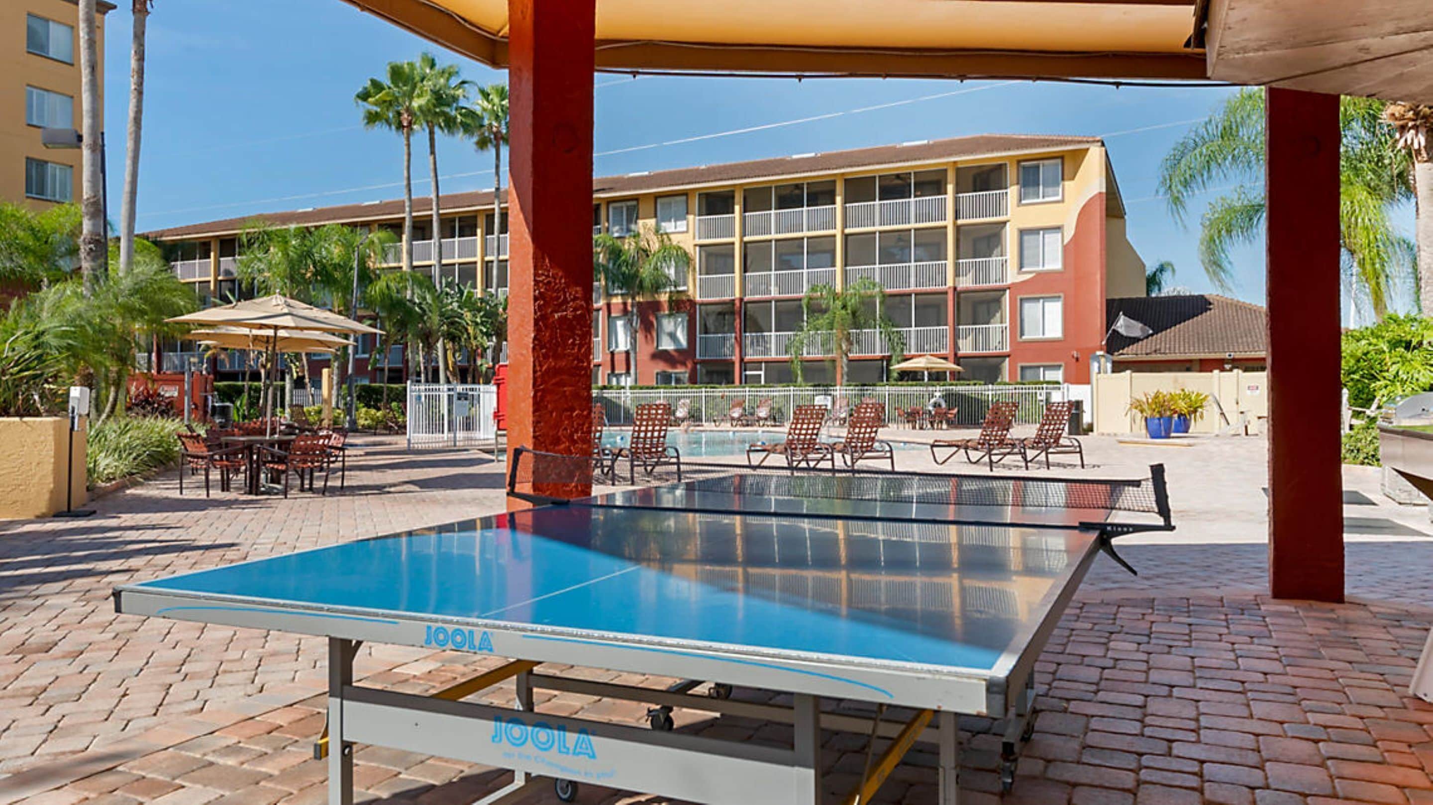 A pool table under a canopy with a view of a multi-story building in the background.
