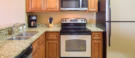 A kitchen with wooden cabinets, a stainless steel microwave, a built-in oven, a refrigerator, granite countertops, and a coffee maker.