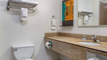 Un baño con inodoro, lavamanos, perchero para toallas y un cuadro en la pared.