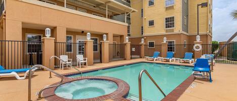 A pool area with lounge chairs and a hot tub, surrounded by a multi-story building with balconies.