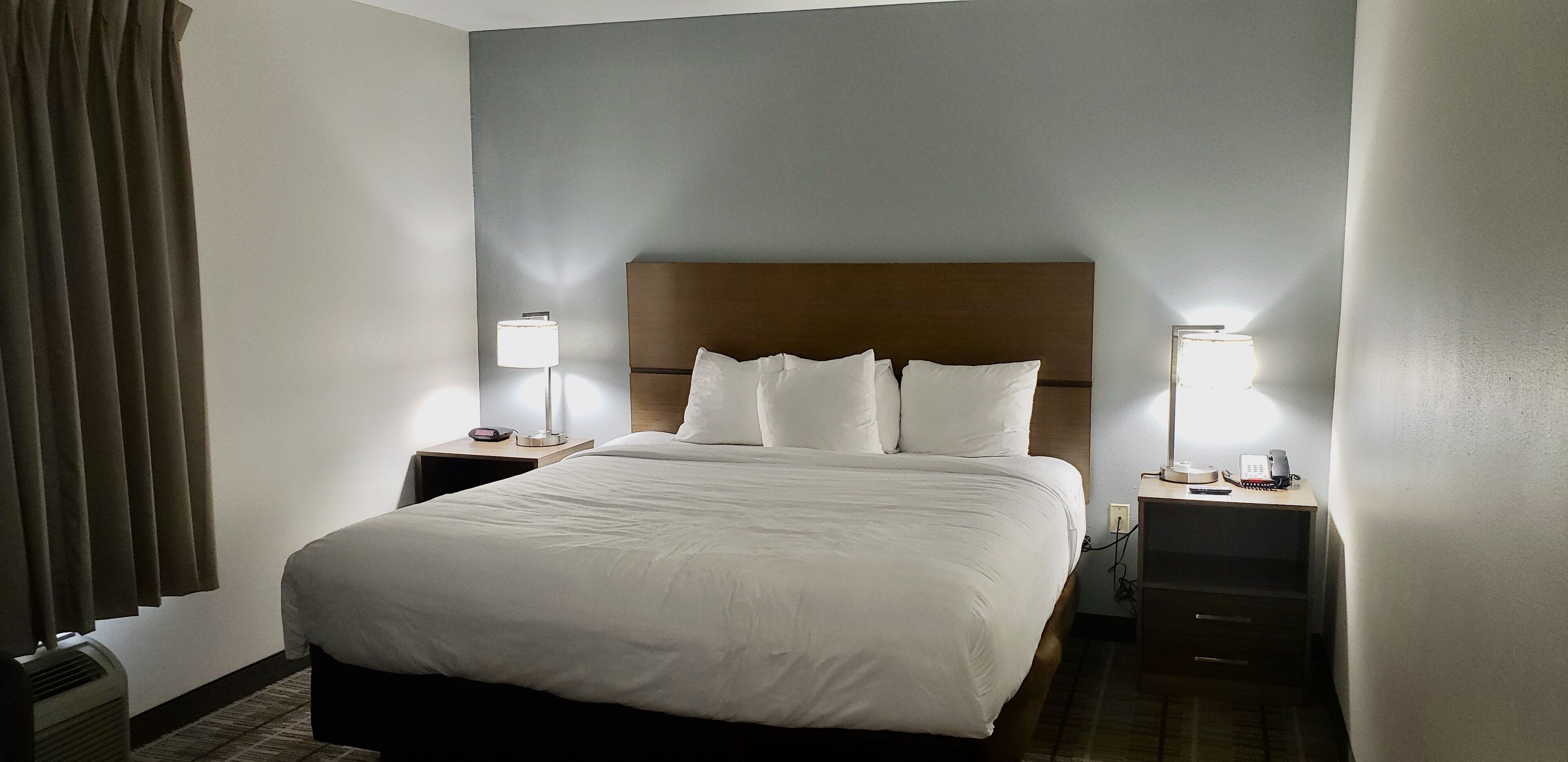 A hotel room with a large bed, two bedside tables with lamps, a heater, and a telephone.