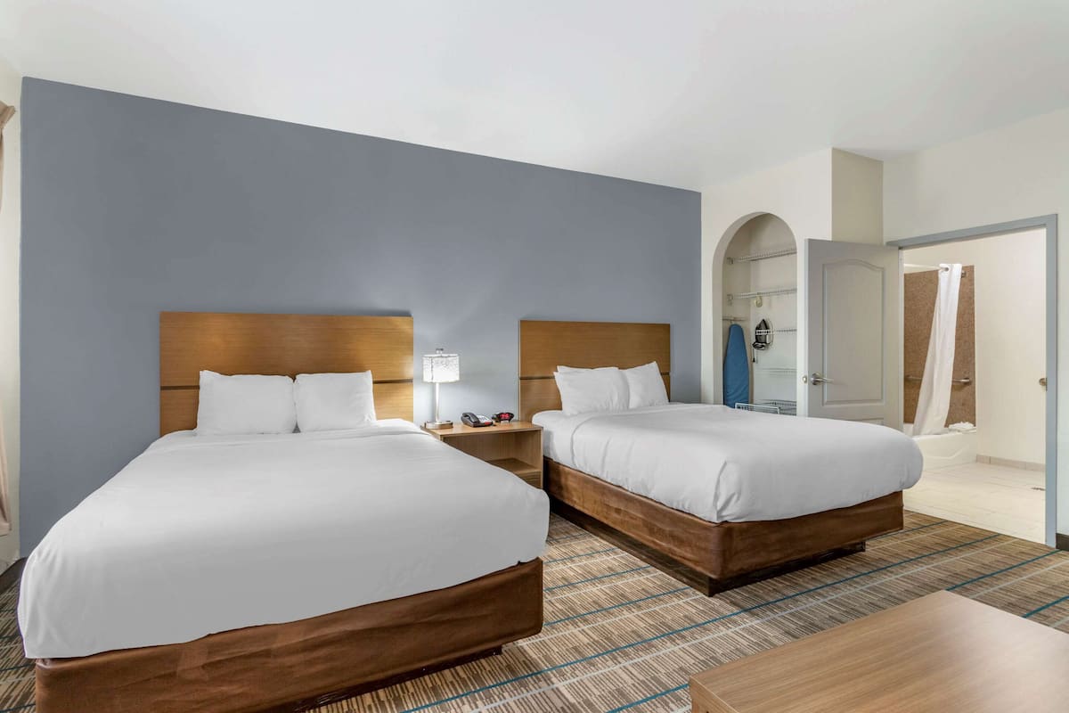 Et hotelværelse med to senge, et natbord med en lampe og udsigt til et badeværelse.