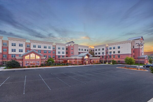 A large hotel with a central building and multiple wings, featuring a spacious parking lot in front.