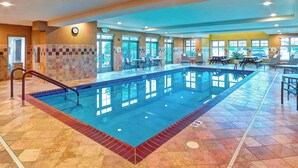 Une piscine intérieure avec un sol carrelé, une horloge au mur et un espace détente avec des tables et des chaises.