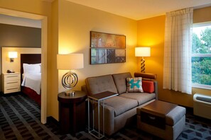 Una habitación de hotel con cama, sofá, una mesita, lámpara y un cuadro en la pared.