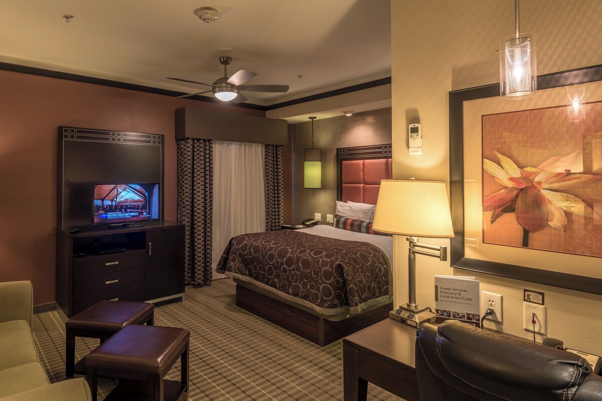 A hotel room with a bed, a TV, a desk, a chair, a ceiling fan, and a lamp.