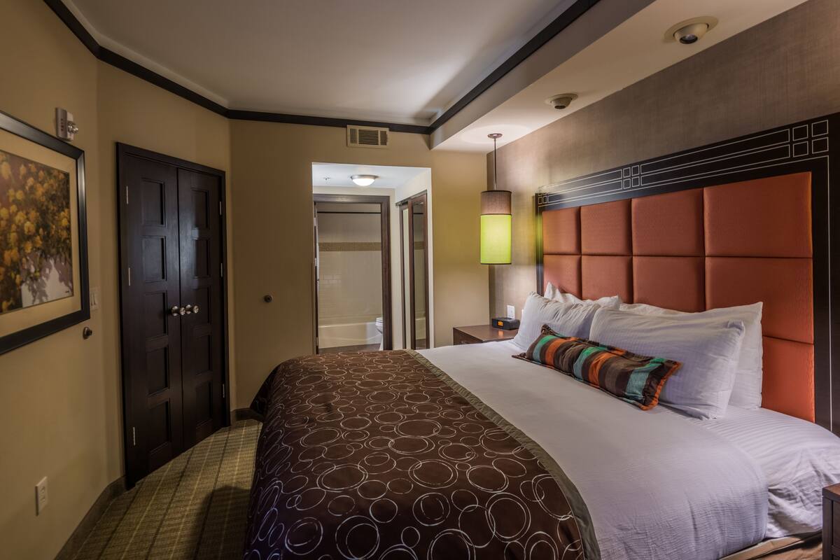 A hotel room with a large bed, a headboard, a nightstand, a lamp, and a door.