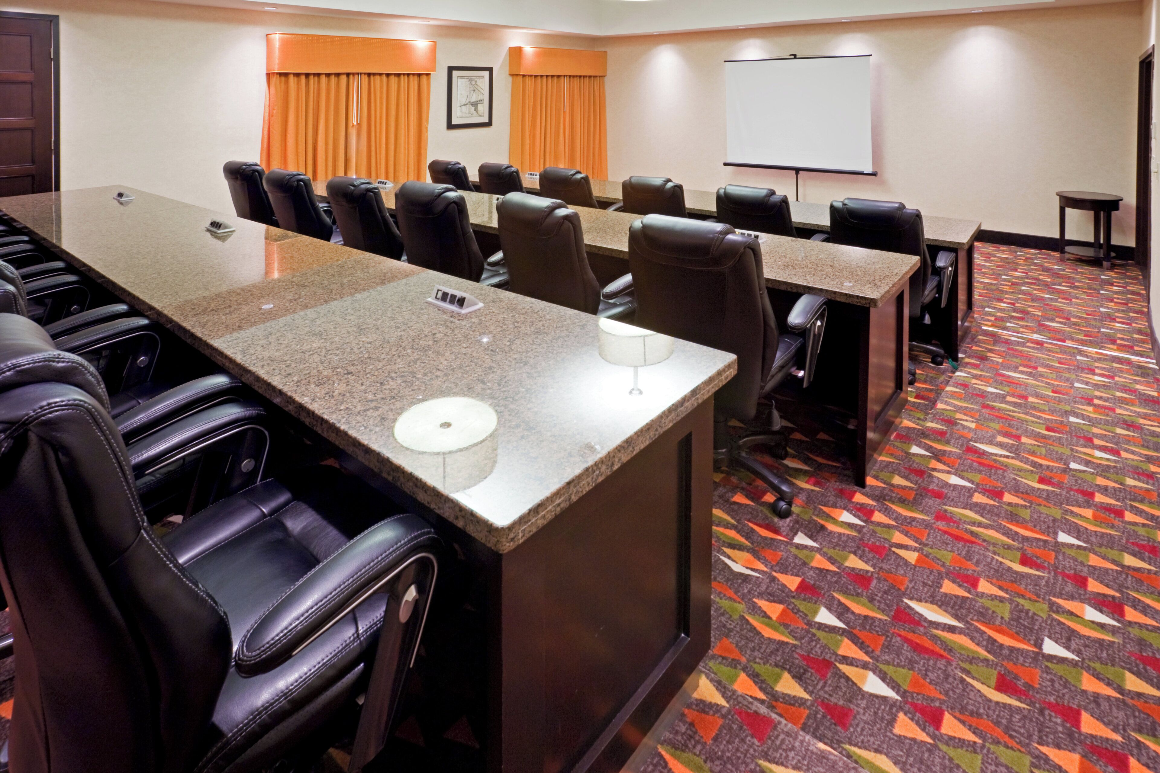 A conference room with multiple tables and chairs, a whiteboard, and a patterned carpet.