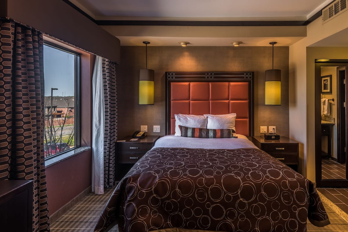 A hotel room with a large bed, a nightstand, a desk, and a view of the outside.