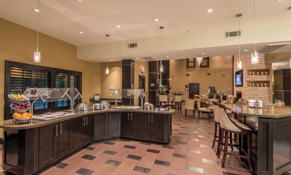A hotel lobby with a central bar area, seating arrangements, and a buffet counter.