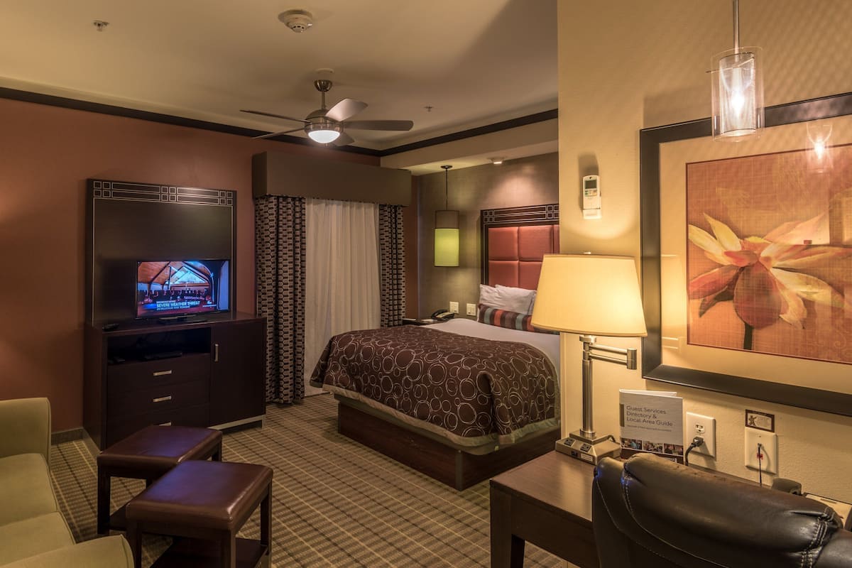 A hotel room with a bed, a TV, a desk, a chair, a ceiling fan, and a lamp.
