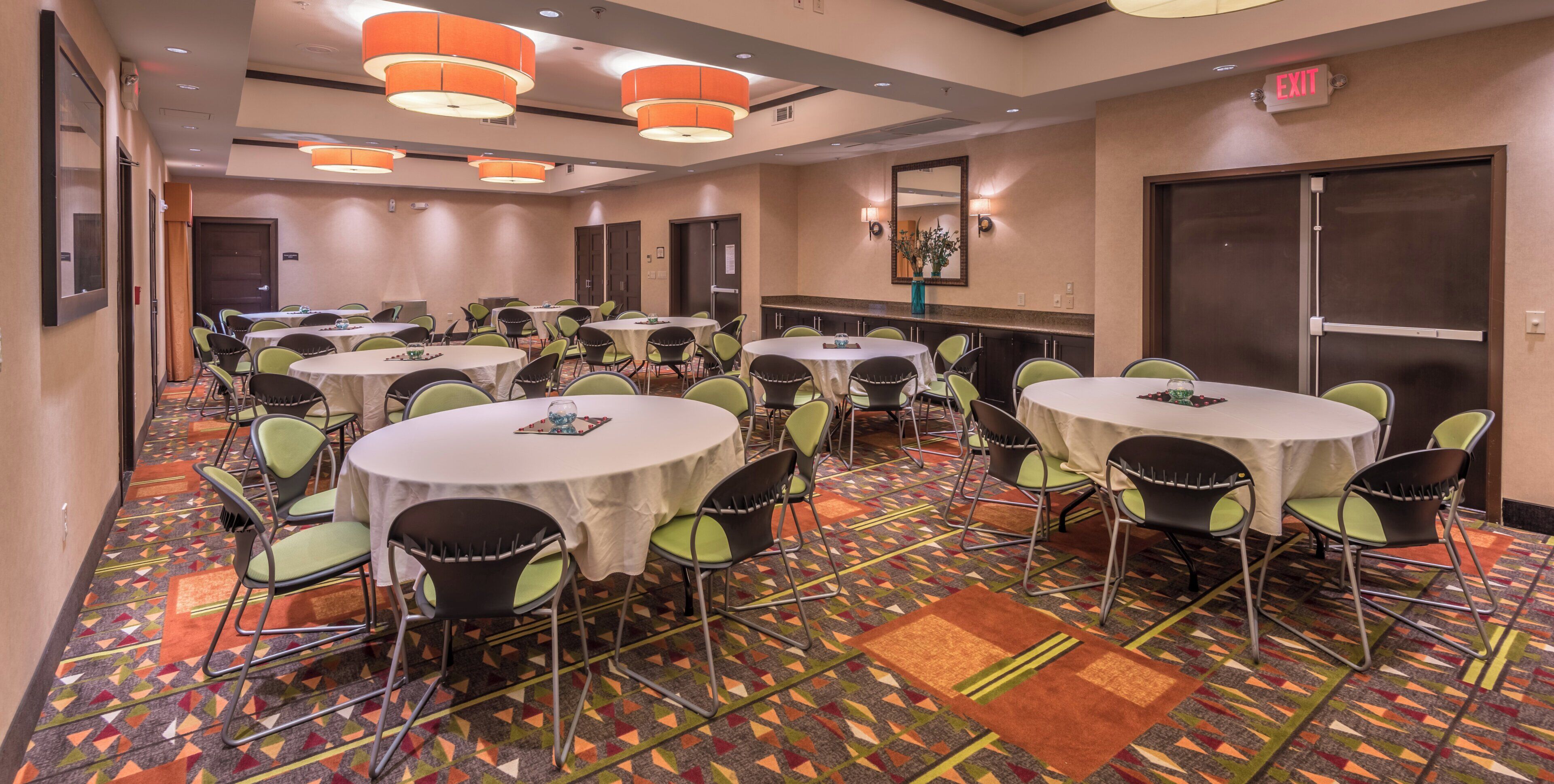 A hotel conference room with multiple round tables, green chairs, and patterned carpet.