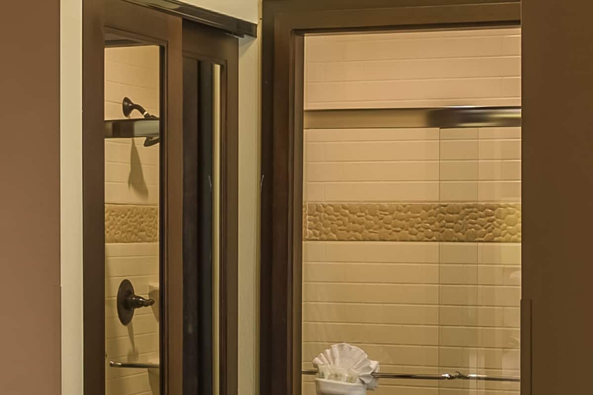 A bathroom with a toilet, a shower with a towel rack, and a mirror reflecting the room.