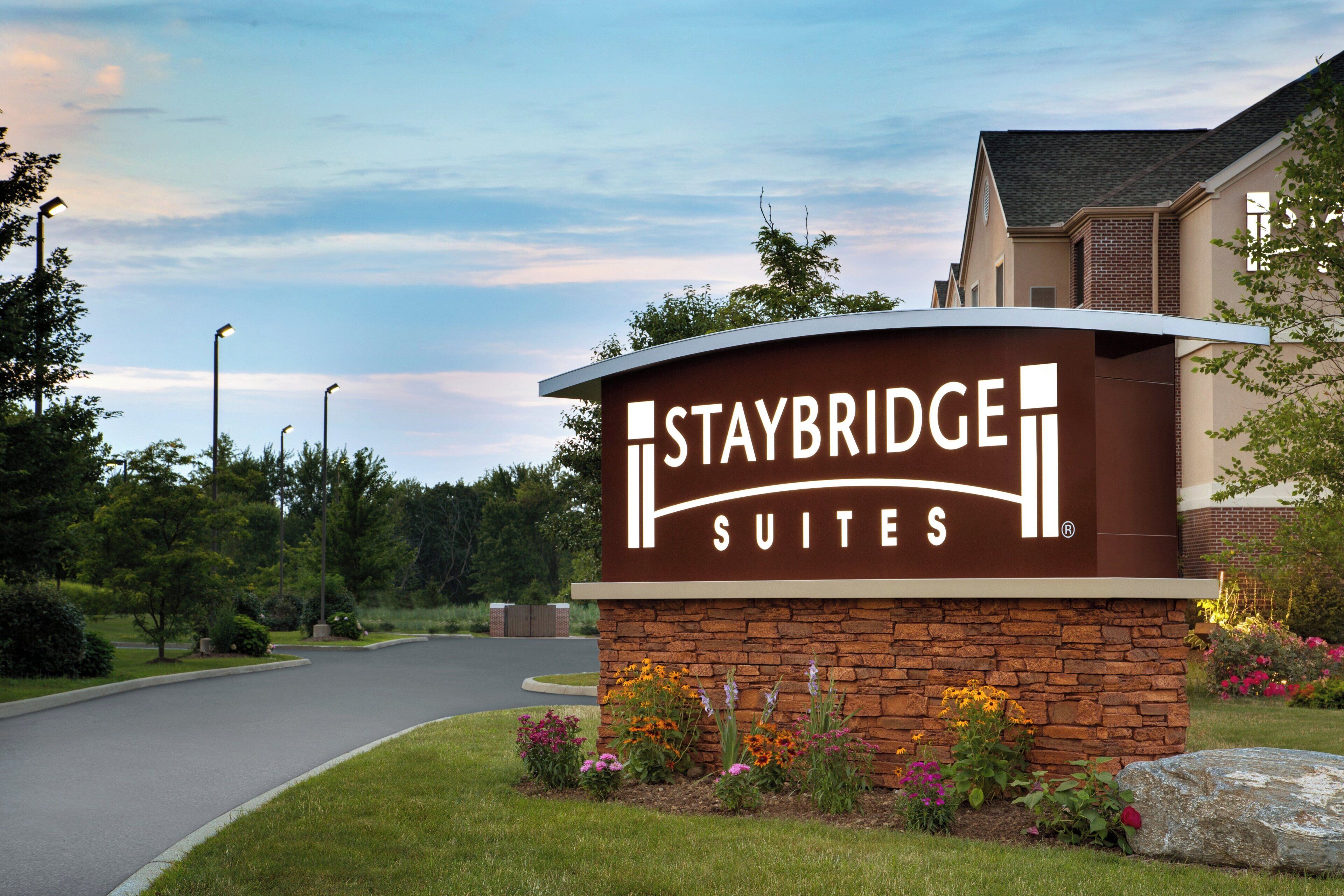 A sign for Staybridge Suites with a brick base and a curved top.