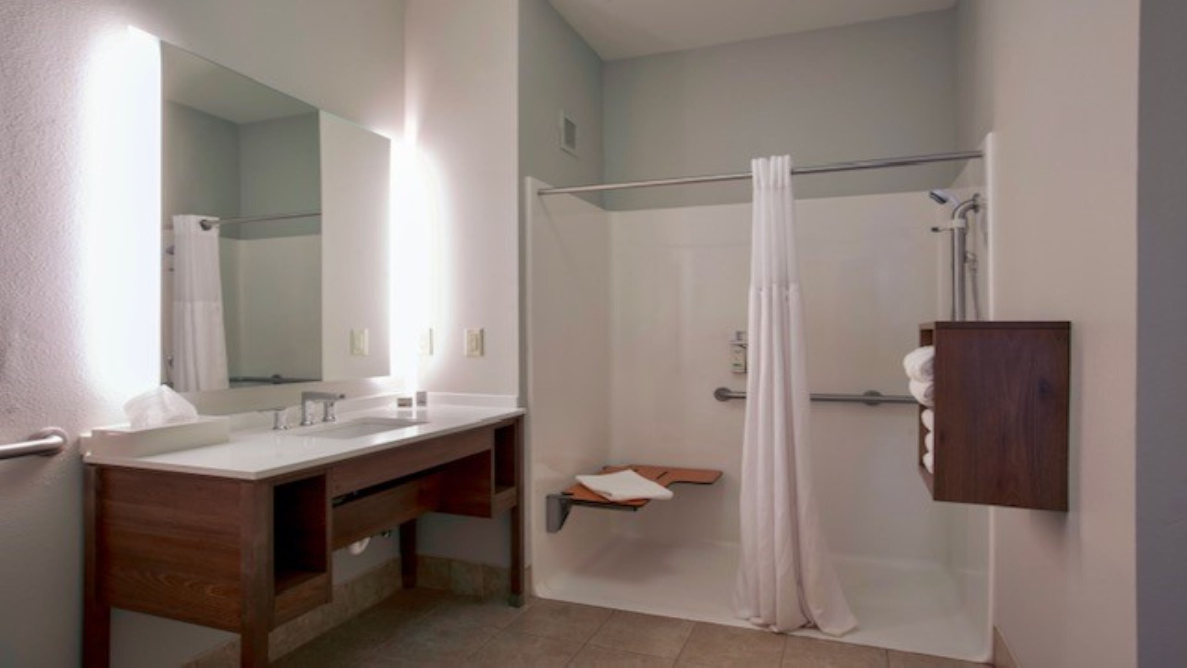 Une salle de bain avec un meuble-lavabo en bois, un grand miroir, une douche avec un rideau et un porte-serviettes.