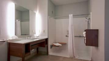 Une salle de bain avec un meuble-lavabo en bois, un grand miroir, une douche avec un rideau et un porte-serviettes.
