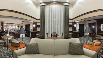 Un vestíbulo de hotel con un área de estar central, un bar y un comedor.
