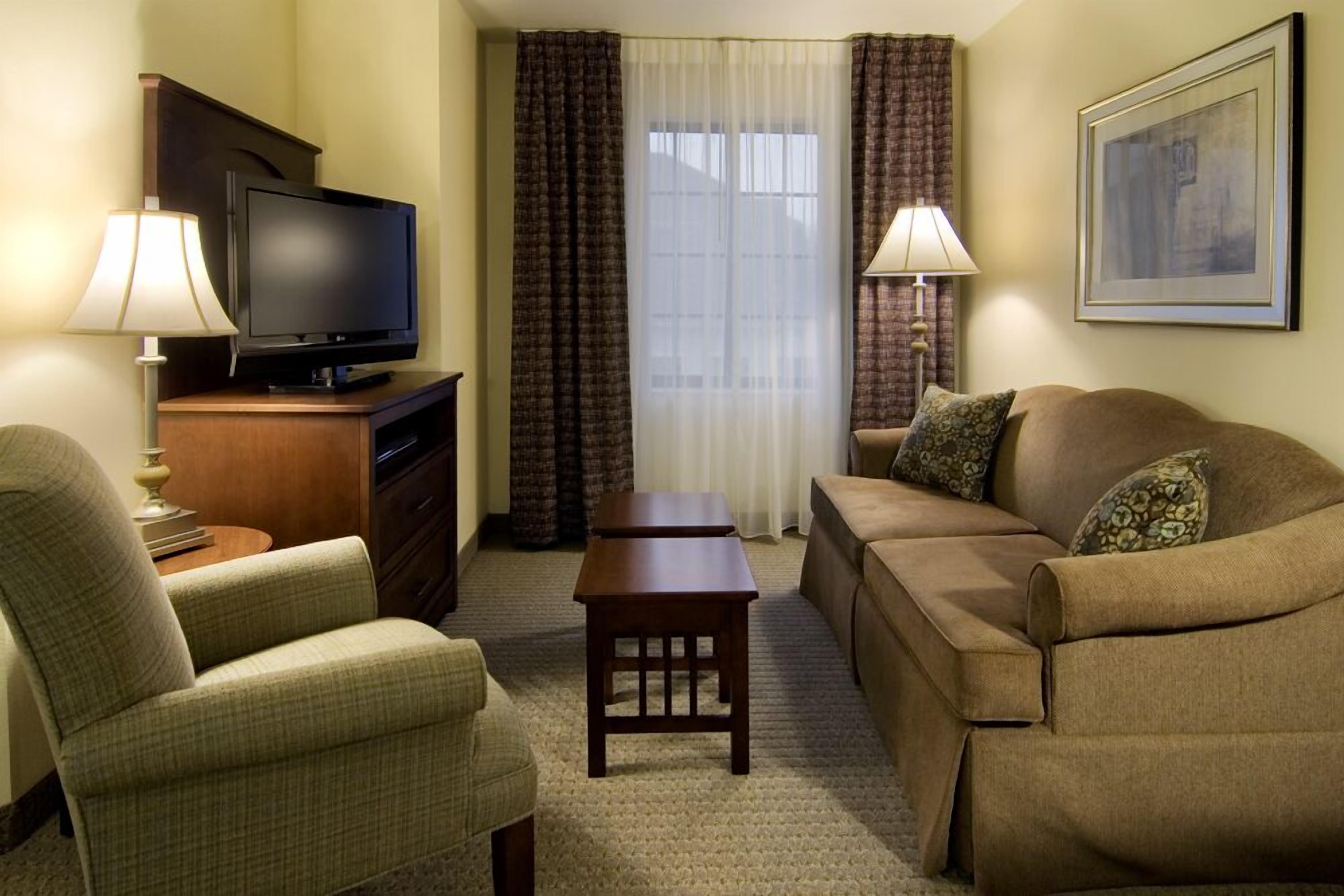 A hotel room with a television, two lamps, a sofa, a chair, and a small table.