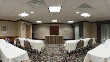 A conference room with a central table, four tables with chairs, and a patterned carpet.