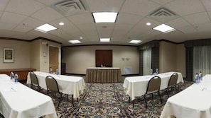 Un salón de conferencias con una mesa central, cuatro mesas con sillas y una alfombra estampada.