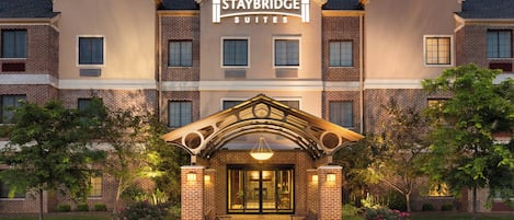 Un hotel Staybridge Suites con fachada de ladrillo, una entrada central con dosel y un camino de entrada ajardinado.