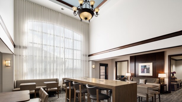 A hotel lobby with a long wooden reception desk, several seating areas including a sofa and chairs, and a large window with sheer curtains. - Staybridge Suites Akron-Stow-Cuyahoga Falls by IHG (Stow)