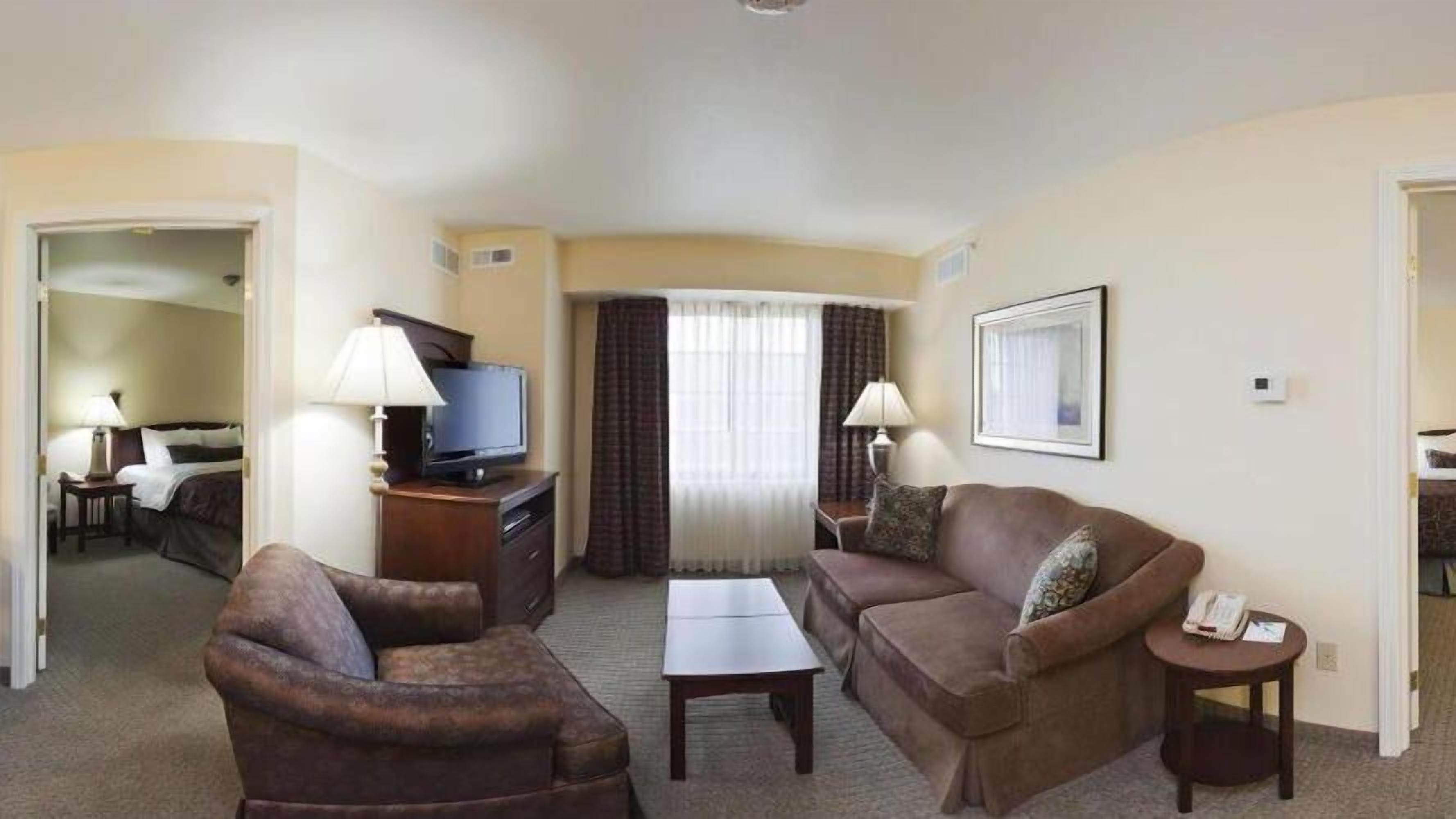 Habitación de hotel con sala de estar que incluye un sofá, un sillón, una mesa de centro, un televisor y una mesita auxiliar.