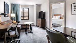 Een hotelkamer met een bed, een bureau, een stoel, een televisie en een raam met gordijnen.