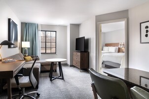 Quarto de hotel com cama, escrivaninha, cadeira, televisão e janela com cortinas.