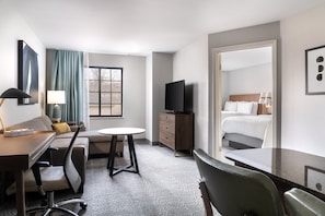 Habitación de hotel con cama, escritorio, silla, televisor y ventana con cortinas.