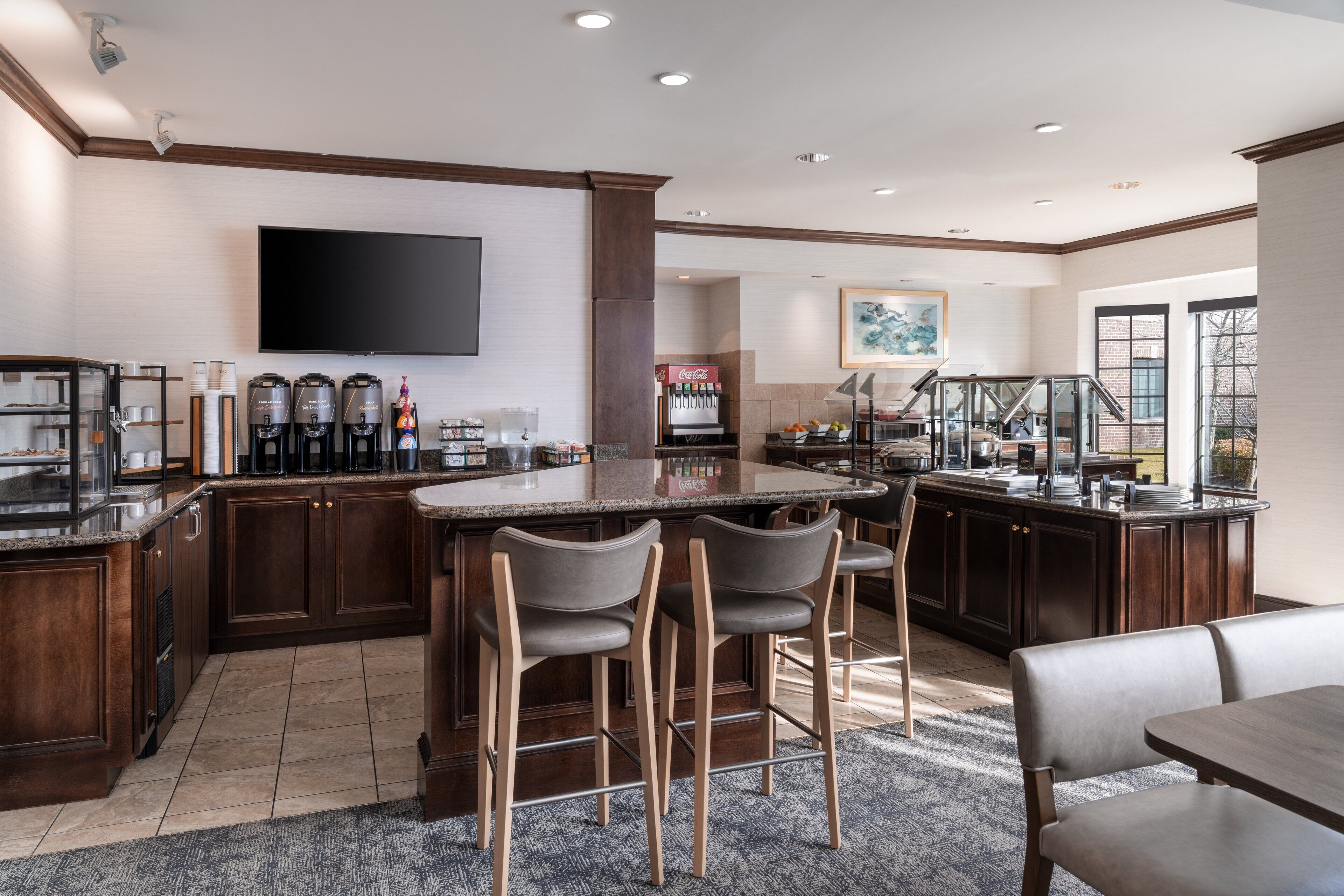 A modern kitchen with a bar area, a flat-screen TV, and a Coca-Cola refrigerator.