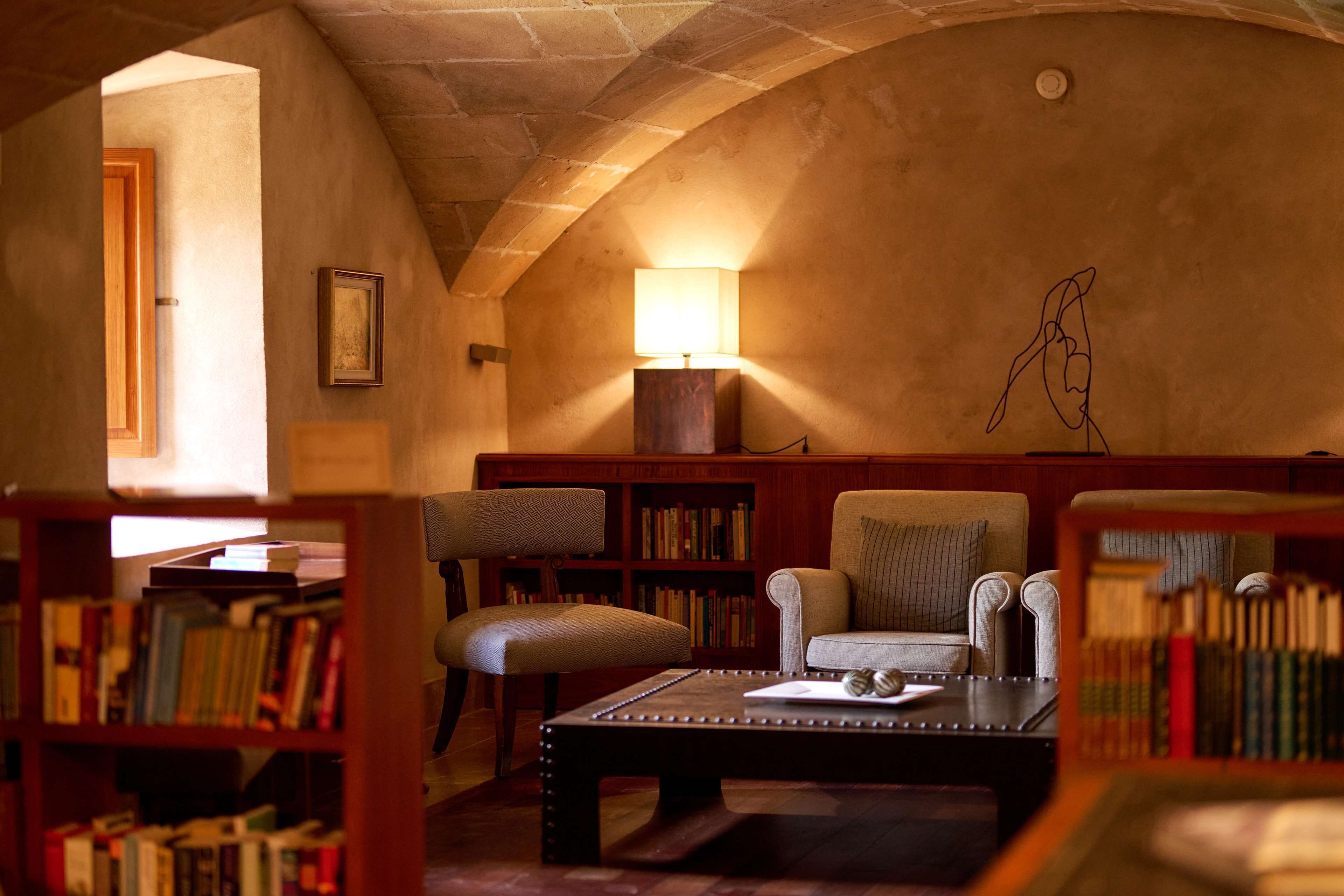 A cozy reading room with a high arched ceiling, a wooden bookshelf, a comfortable armchair, and a coffee table.