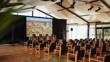 A conference room with rows of chairs, a large screen, and a view of a cityscape through large windows.