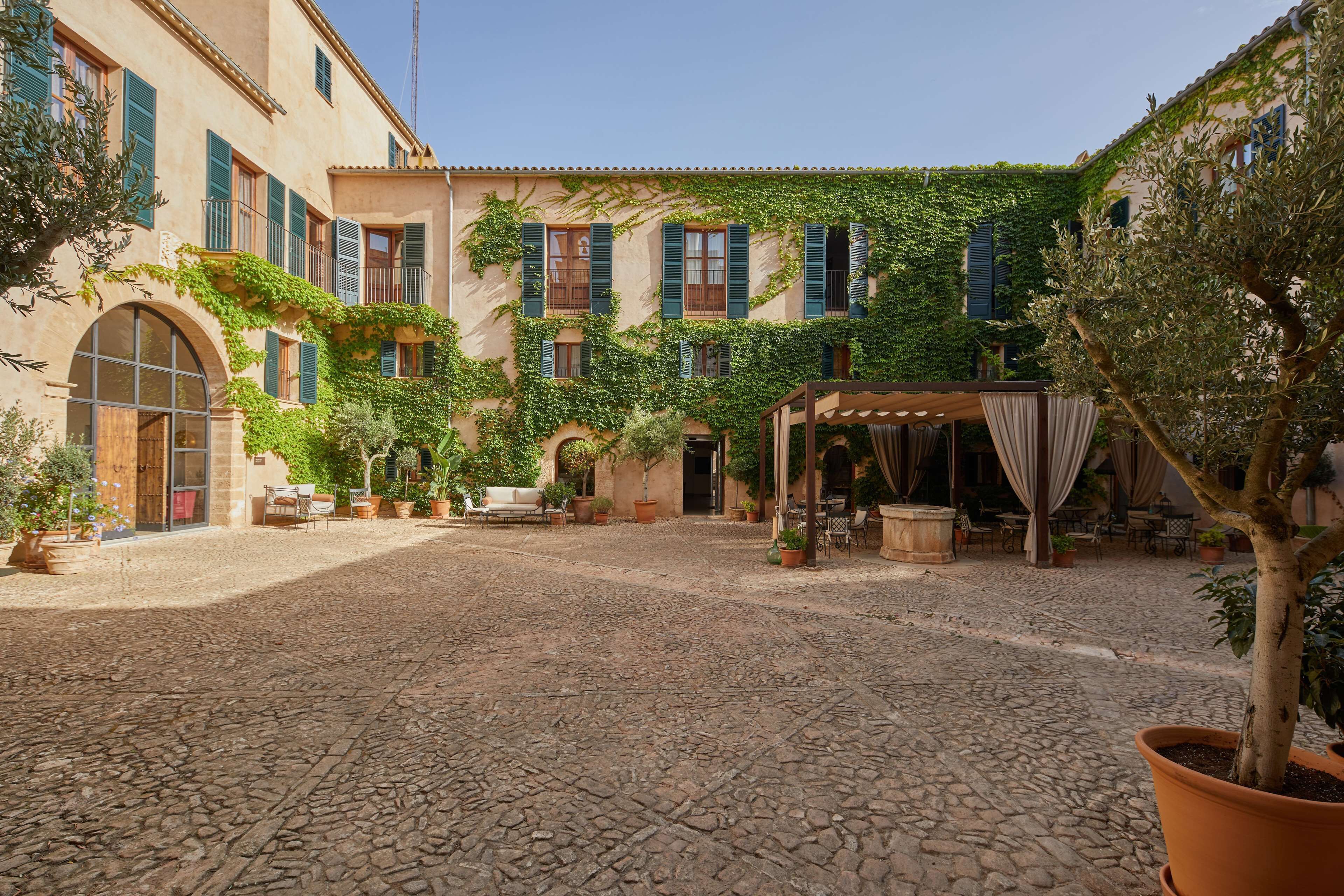 Un patio con suelo de adoquines, mobiliario exterior y una zona cubierta con cortinas.