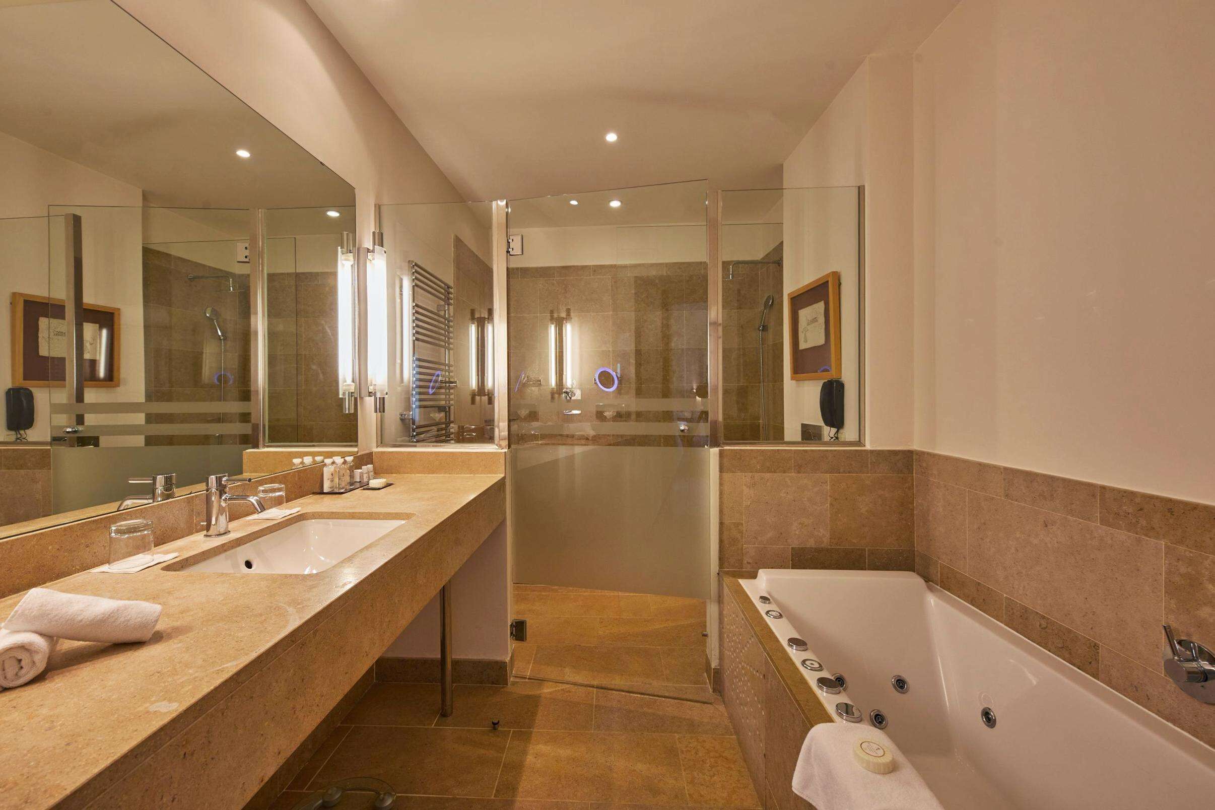 A modern bathroom with a large mirror, two sinks, a shower enclosure, and a bathtub.