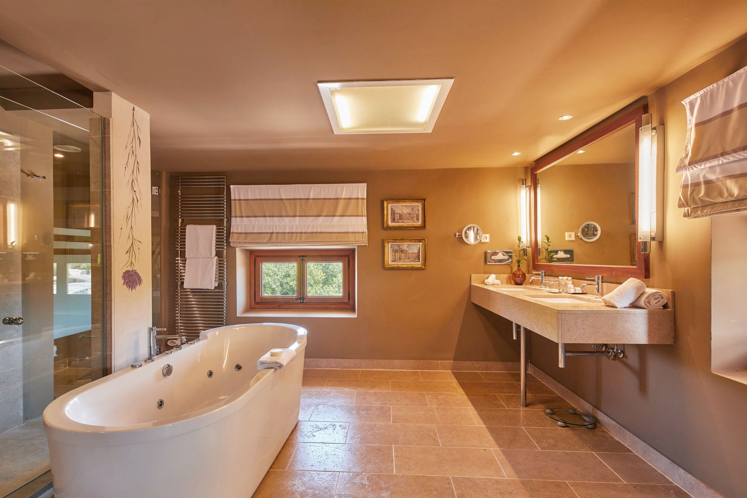 Un bagno moderno con una vasca freestanding, un ampio mobile lavabo con specchio e una finestra che lascia entrare luce naturale.