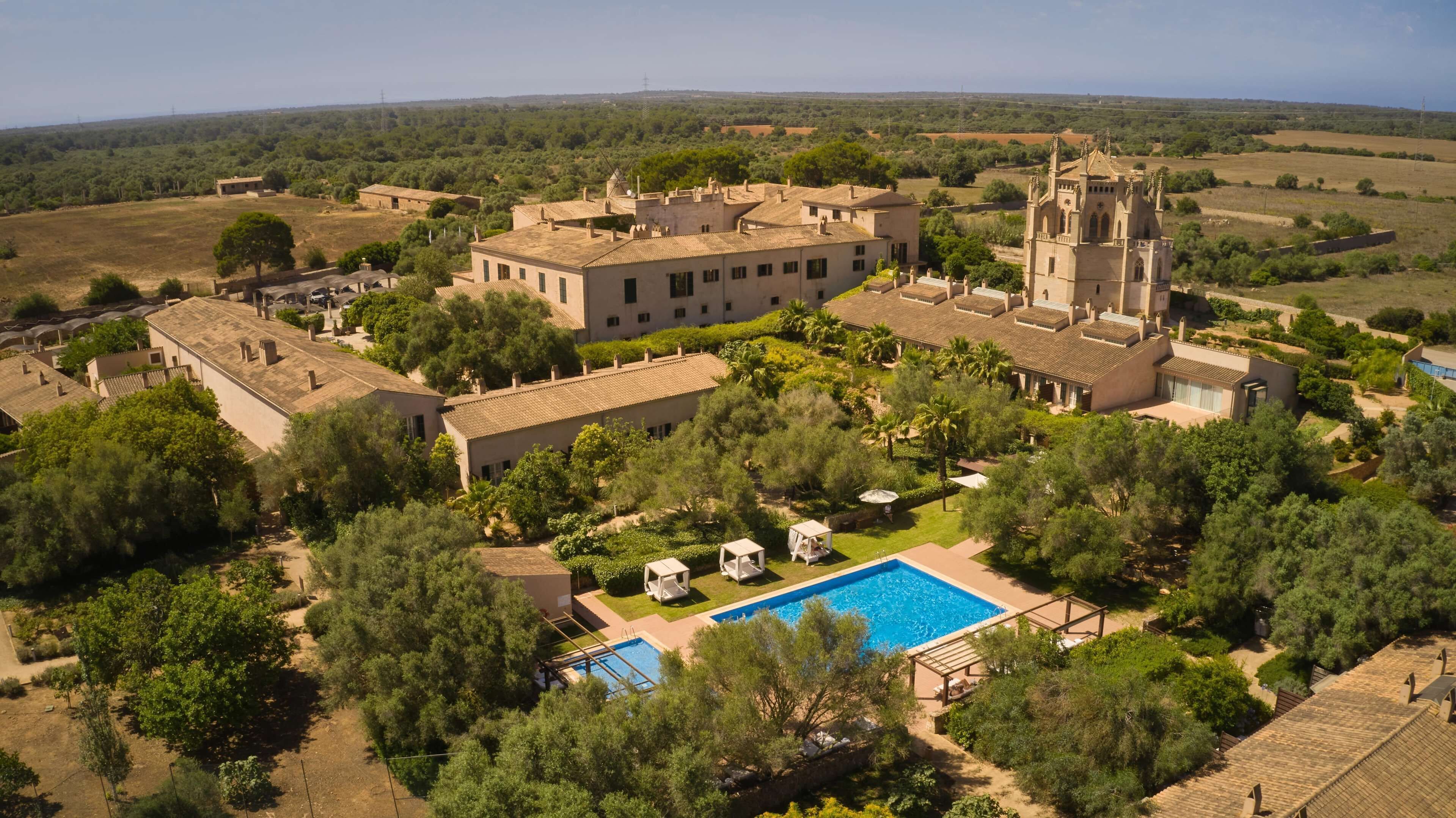 An aerial view of a resort with a swimming pool, lush greenery, and a prominent church-like building.