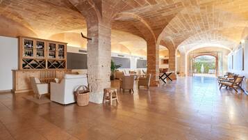A spacious interior with a high ceiling and arched brick design, featuring a seating area with a wooden cabinet displaying bottles.