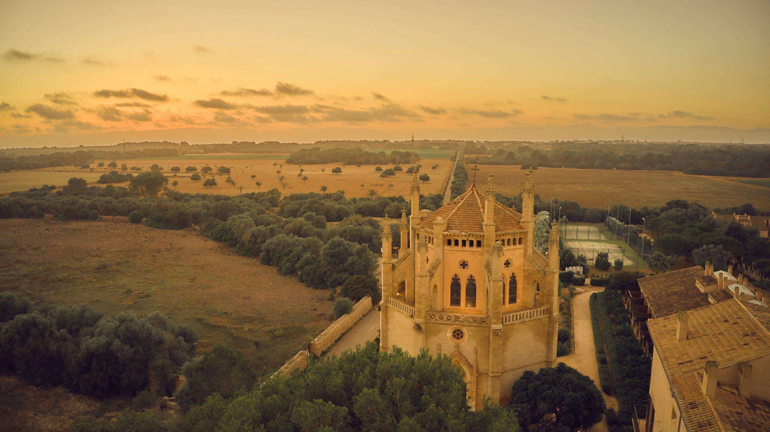 A historic church with a prominent tower, surrounded by open fields and sparse trees.