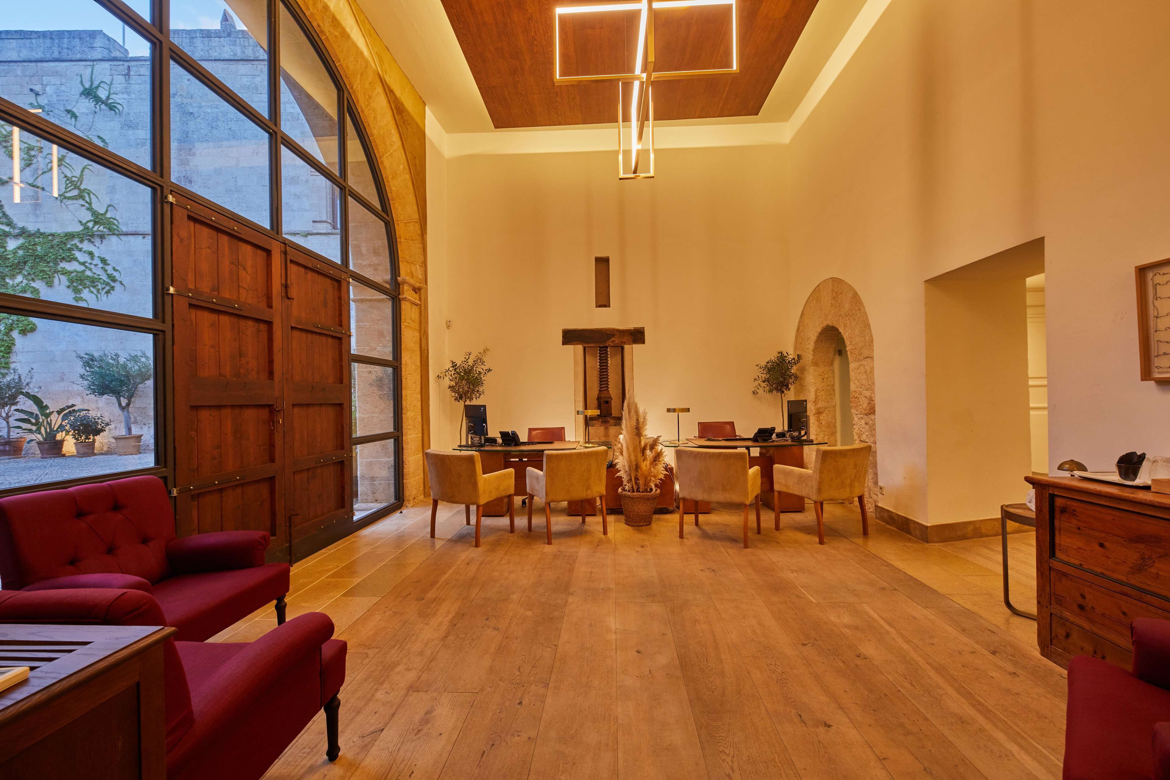 A spacious room with wooden flooring, a large window, and a dining area with chairs and tables.