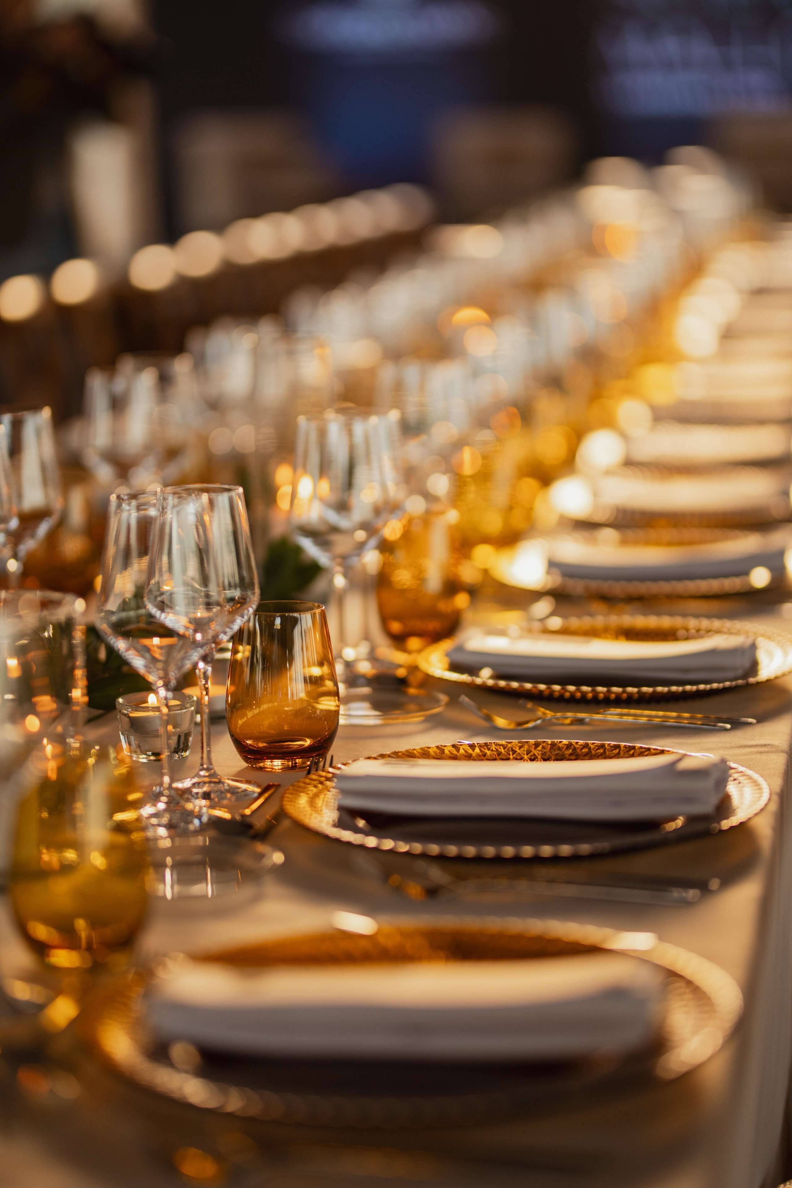 Una larga mesa dispuesta con numerosas copas de vino, platos y cubiertos, lo que sugiere un ambiente de comedor formal.