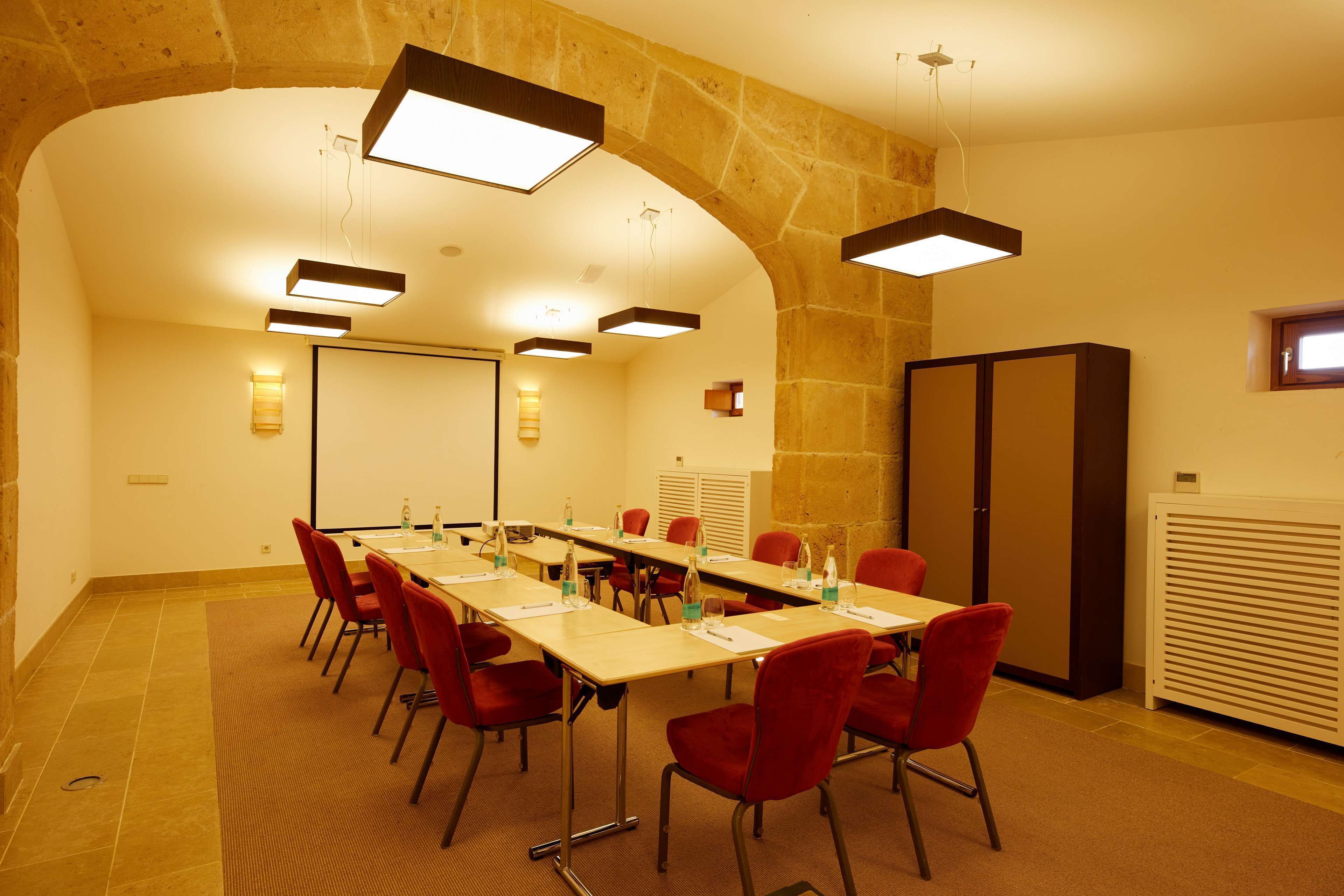 Une salle de conférence avec une longue table, des chaises rouges et des luminaires modernes.
