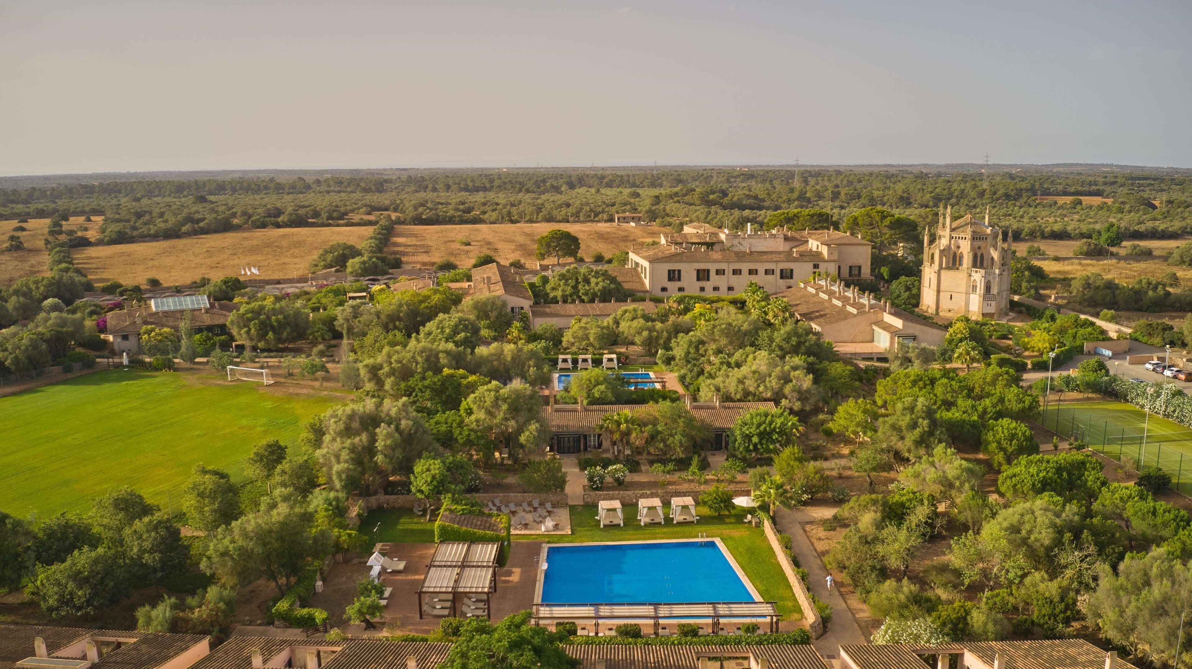 Vista aèria d'una extensa finca amb piscina, pistes de tennis i una església amb campanar.
