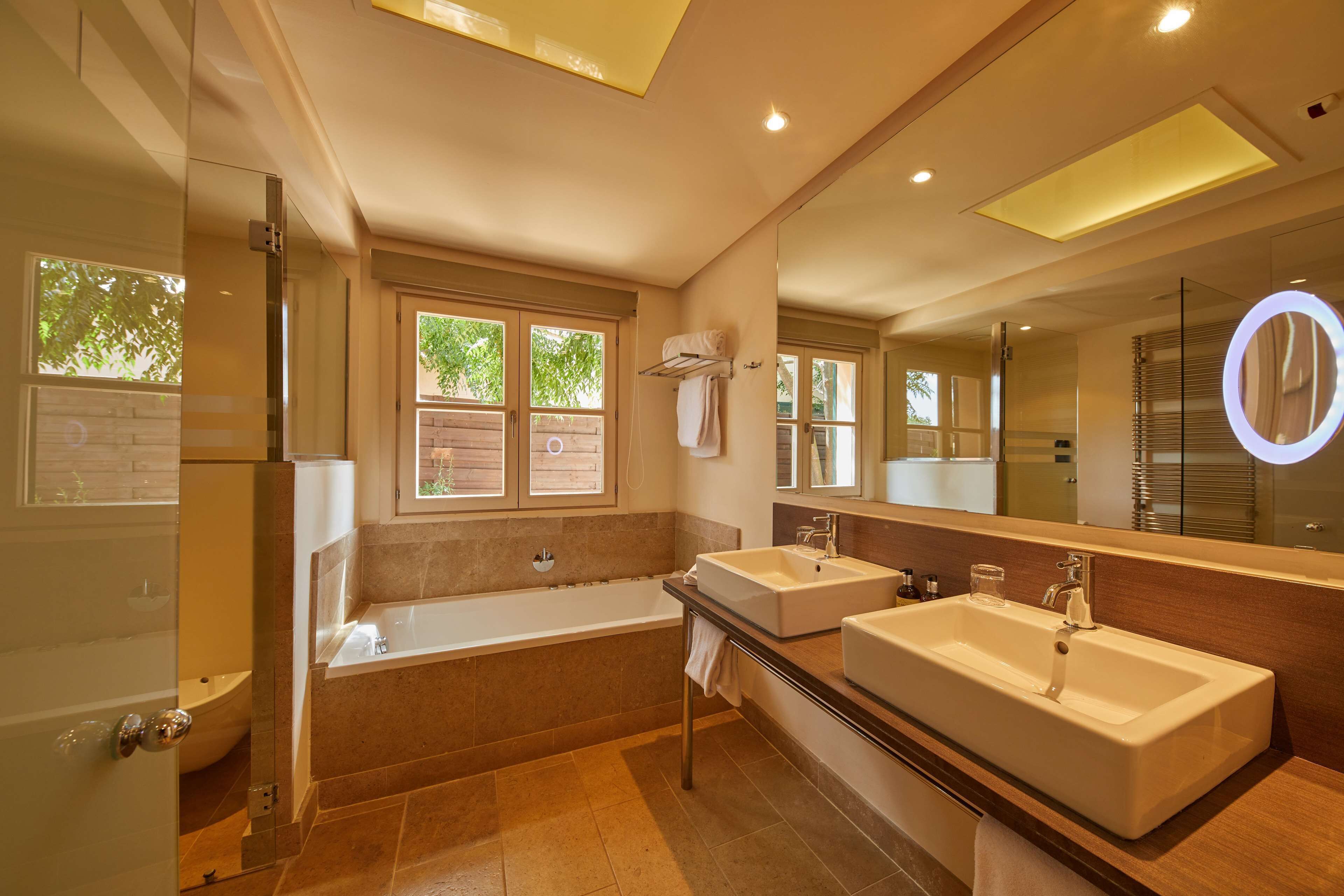A modern bathroom with a bathtub, two sinks, a large mirror, and a glass shower enclosure.