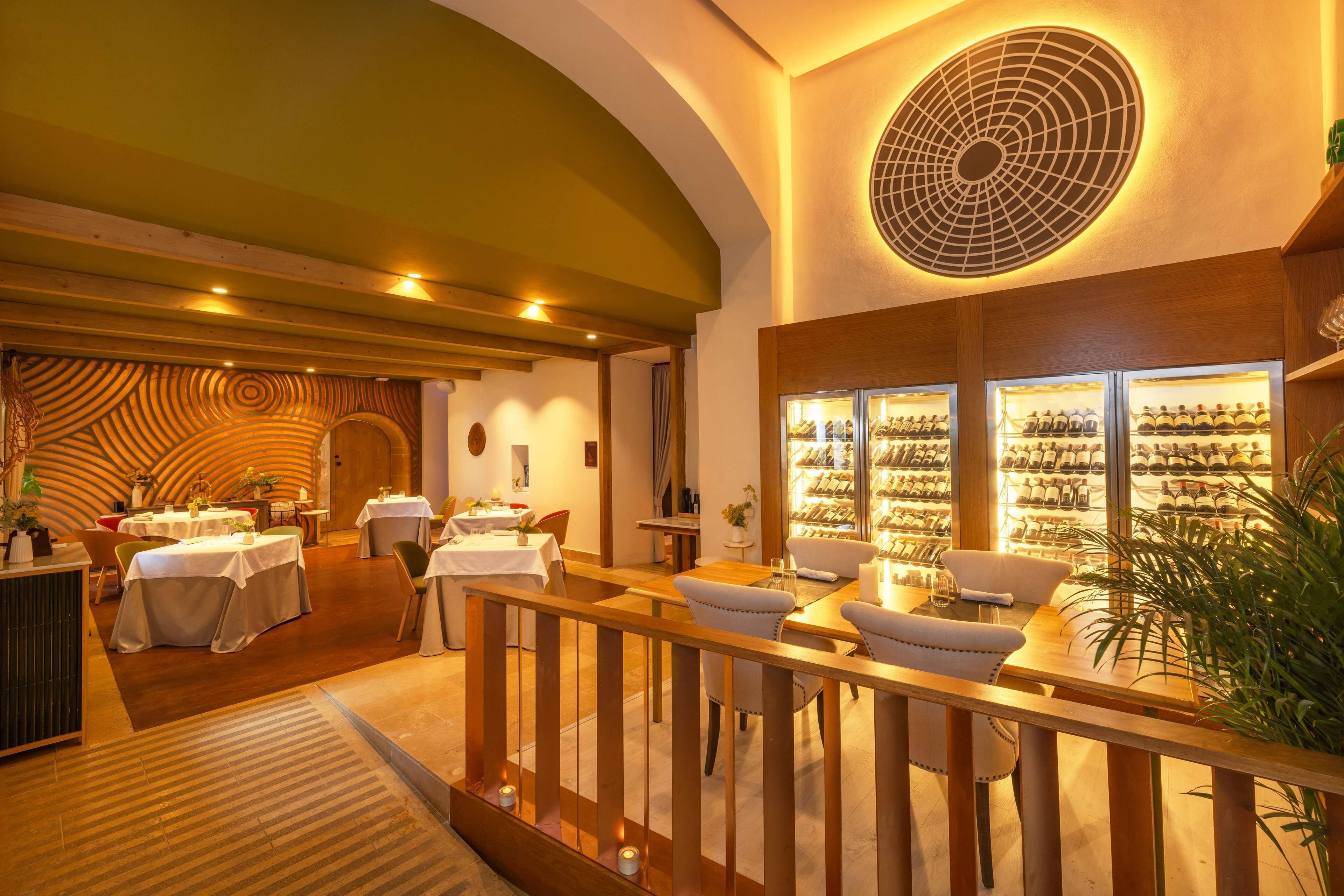 A restaurant with a warm interior, wooden furniture, and a wine display.