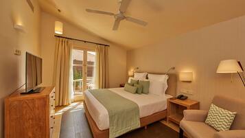 Una habitación de hotel con cama, televisión, escritorio, silla y ventilador de techo.