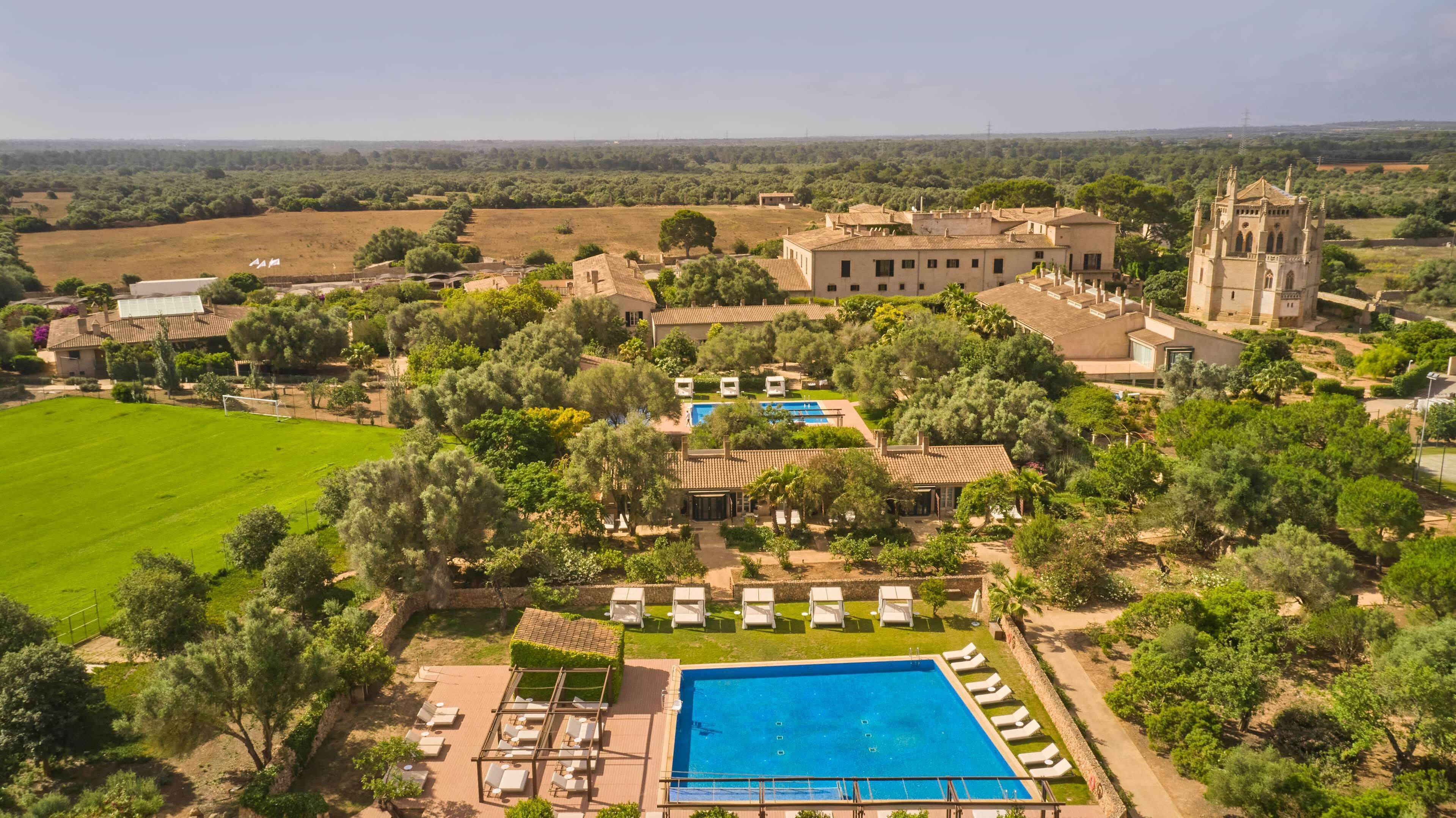 Vista aérea de um resort com piscina, áreas de descanso e um edifício grande com uma torre.